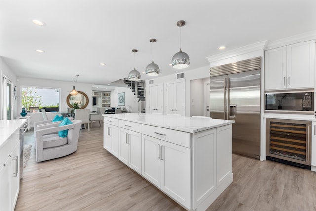 kitchen featuring built in appliances, white cabinets, pendant lighting, light stone counters, and beverage cooler