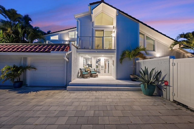 back house at dusk featuring a balcony and a garage