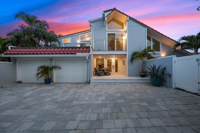 back house at dusk featuring a balcony and a garage