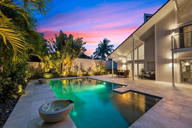 pool at dusk with an in ground hot tub and a patio area