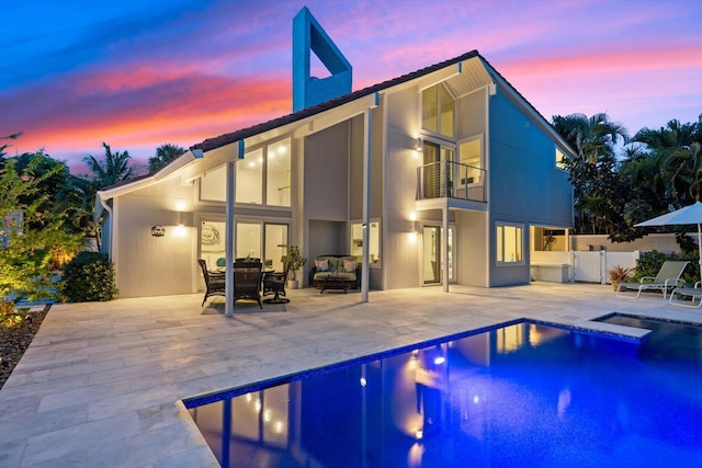 back house at dusk featuring a balcony, a fenced in pool, and a patio area