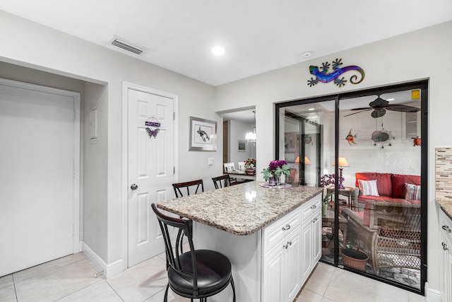 kitchen featuring light tile patterned flooring, white cabinetry, a breakfast bar, and light stone counters