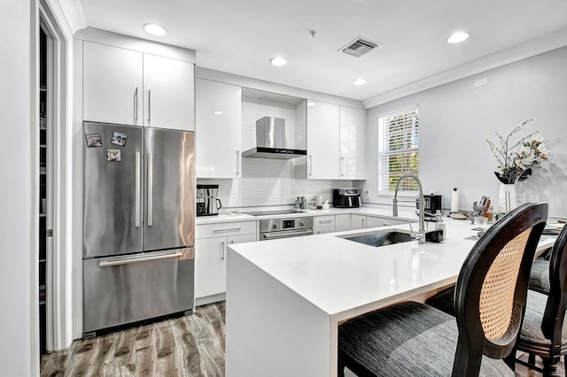 kitchen featuring appliances with stainless steel finishes, sink, white cabinetry, wall chimney range hood, and ornamental molding