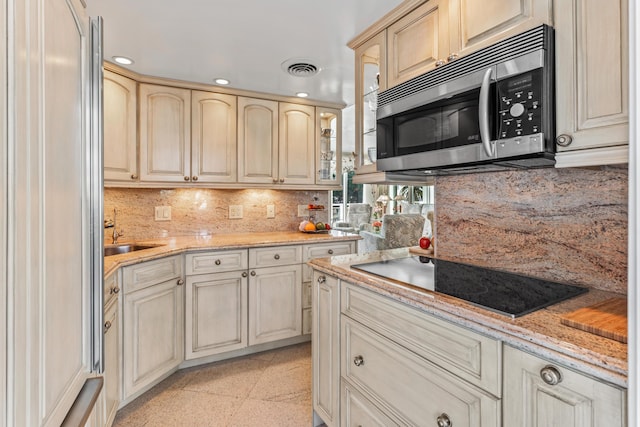 kitchen featuring light stone counters, black electric stovetop, sink, and backsplash