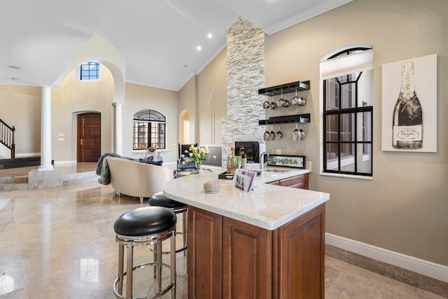 kitchen with a breakfast bar, decorative columns, a high ceiling, light stone counters, and an island with sink