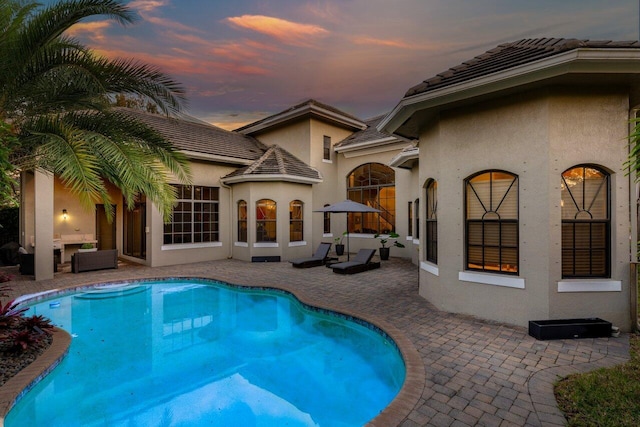 pool at dusk featuring an outdoor hangout area and a patio