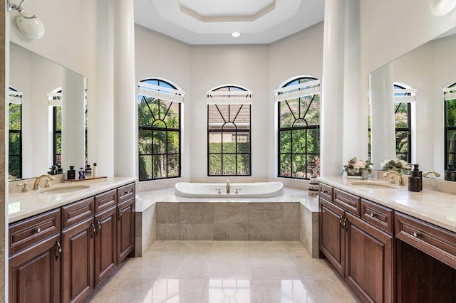 bathroom featuring a relaxing tiled tub, vanity, a tray ceiling, and a wealth of natural light