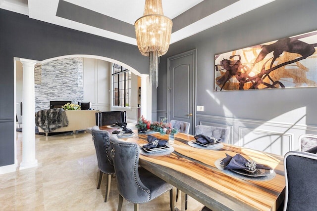 dining room featuring an inviting chandelier, a fireplace, and ornate columns