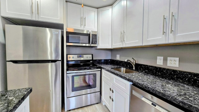 kitchen with light hardwood / wood-style floors, appliances with stainless steel finishes, white cabinetry, sink, and dark stone countertops