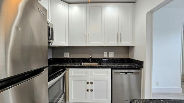 kitchen with white cabinets, appliances with stainless steel finishes, dark stone countertops, sink, and hardwood / wood-style flooring