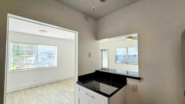 kitchen with ceiling fan, light hardwood / wood-style floors, white cabinets, and dark stone countertops