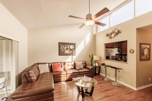 living room with ceiling fan with notable chandelier, sink, a towering ceiling, and light wood-type flooring