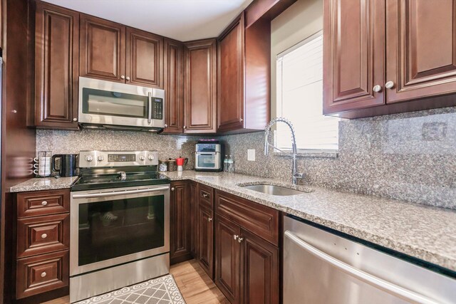 kitchen with sink, tasteful backsplash, light stone countertops, and appliances with stainless steel finishes