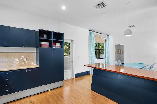 kitchen with light hardwood / wood-style flooring, hanging light fixtures, blue cabinetry, and decorative backsplash