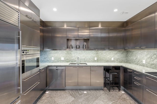 kitchen featuring sink, backsplash, stainless steel appliances, light stone counters, and dark brown cabinetry