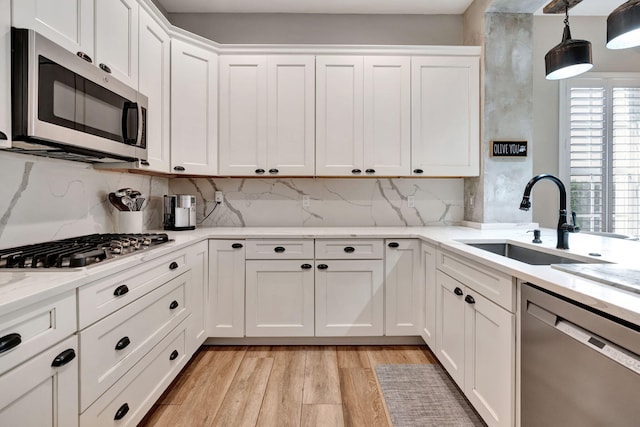 kitchen with sink, white cabinets, hanging light fixtures, stainless steel appliances, and light wood-type flooring