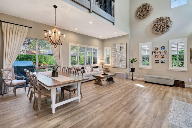 dining area featuring a notable chandelier, a towering ceiling, a wealth of natural light, and light hardwood / wood-style floors