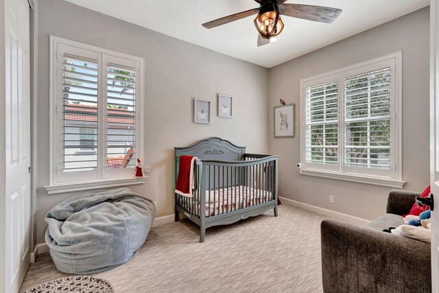 bedroom with ceiling fan, light colored carpet, a textured ceiling, and a crib