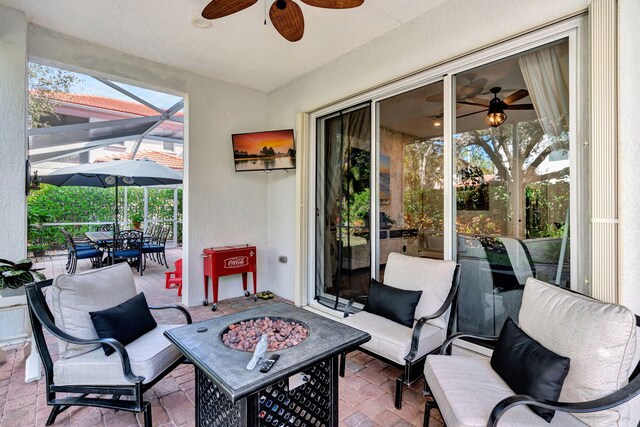 view of patio / terrace featuring ceiling fan, glass enclosure, and a fire pit