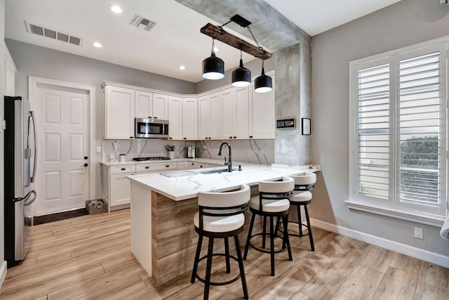 kitchen featuring pendant lighting, white cabinetry, a breakfast bar area, kitchen peninsula, and stainless steel appliances