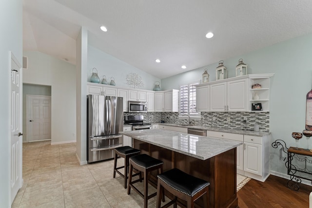 kitchen with white cabinetry, appliances with stainless steel finishes, a kitchen island, and vaulted ceiling