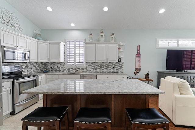 kitchen with a kitchen island, white cabinetry, a kitchen bar, and appliances with stainless steel finishes