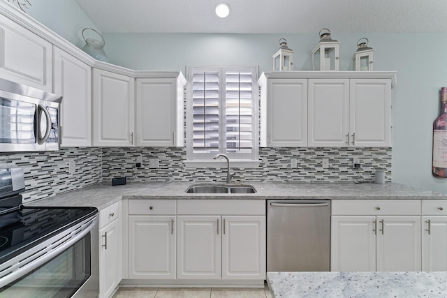 kitchen featuring appliances with stainless steel finishes, white cabinetry, tasteful backsplash, sink, and light tile patterned flooring