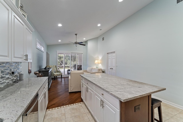 kitchen featuring vaulted ceiling, white cabinets, light tile patterned floors, light stone counters, and a kitchen island