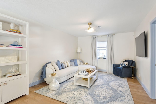 living room with built in features, ceiling fan, and light hardwood / wood-style flooring