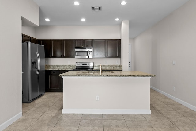 kitchen featuring sink, stainless steel appliances, light stone counters, dark brown cabinetry, and an island with sink