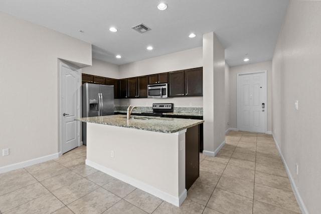 kitchen featuring appliances with stainless steel finishes, sink, a kitchen island with sink, light stone countertops, and dark brown cabinets