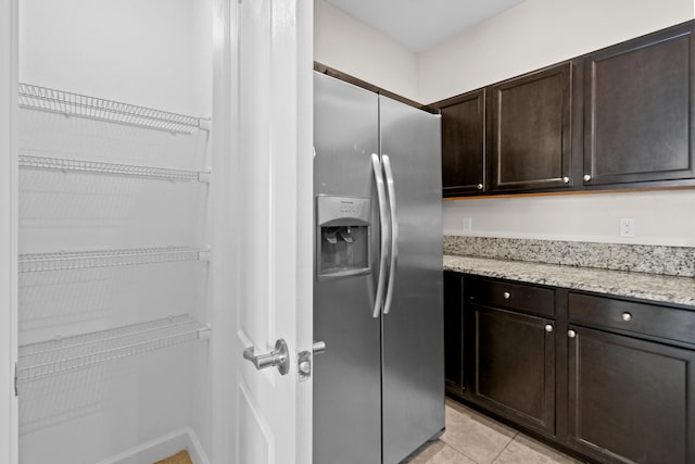 kitchen featuring light stone counters, stainless steel fridge with ice dispenser, dark brown cabinetry, and light tile patterned flooring