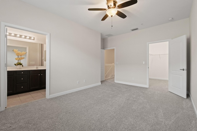 unfurnished bedroom with ensuite bathroom, a spacious closet, light colored carpet, a closet, and ceiling fan