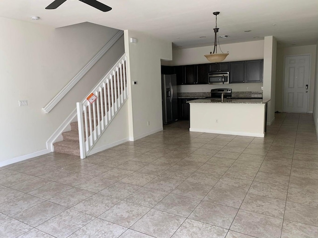 kitchen with pendant lighting, light tile patterned floors, ceiling fan, stainless steel appliances, and a center island with sink