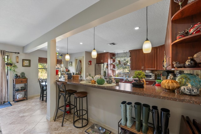 kitchen featuring stainless steel refrigerator with ice dispenser, plenty of natural light, kitchen peninsula, and hanging light fixtures