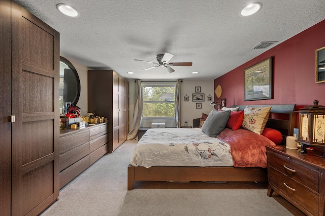 bedroom with ceiling fan, light colored carpet, and a textured ceiling