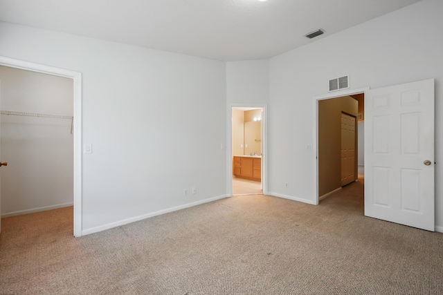 unfurnished bedroom featuring ensuite bathroom, a spacious closet, light carpet, and a closet