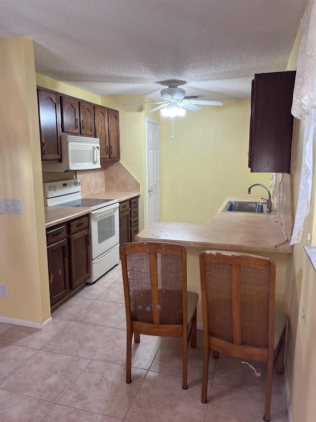 kitchen featuring white appliances, light tile patterned floors, a sink, light countertops, and dark brown cabinetry