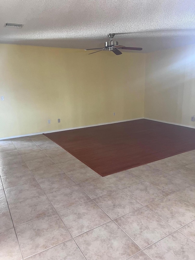 tiled empty room with visible vents, a textured ceiling, and ceiling fan