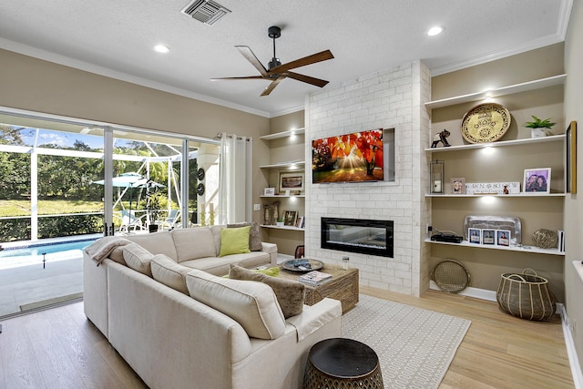 living room with a brick fireplace, ornamental molding, a textured ceiling, and light wood-type flooring