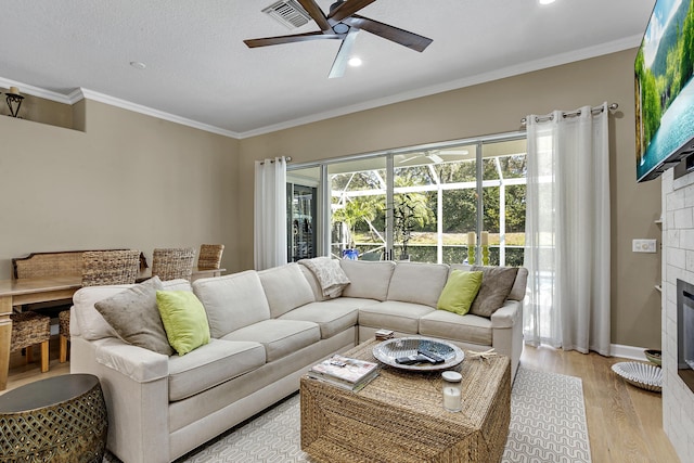 living room featuring ornamental molding, light hardwood / wood-style flooring, a tile fireplace, and ceiling fan