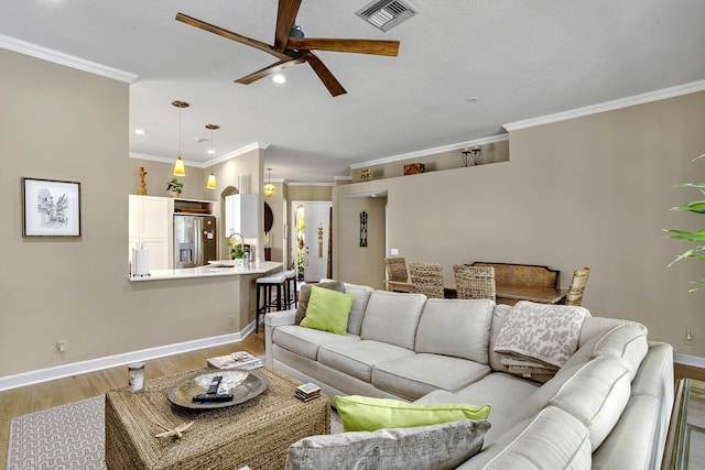 living room featuring ceiling fan, ornamental molding, sink, and light wood-type flooring