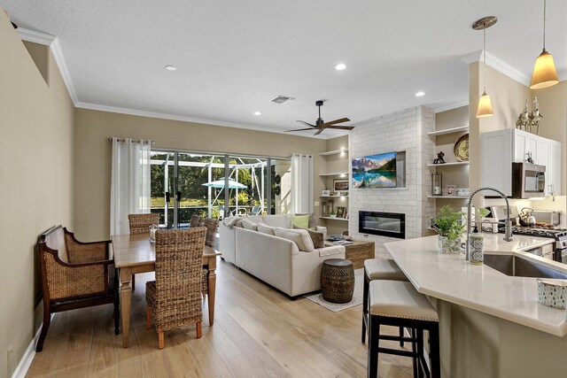 living room with a brick fireplace, a textured ceiling, ornamental molding, ceiling fan, and light hardwood / wood-style floors