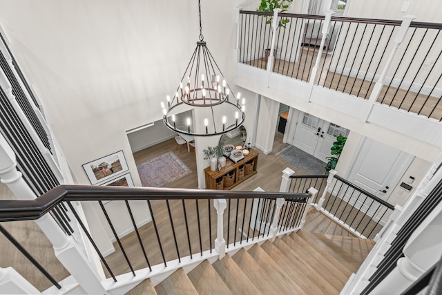 stairway with a high ceiling, hardwood / wood-style floors, and a chandelier