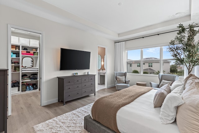 bedroom featuring a closet, a walk in closet, connected bathroom, and light hardwood / wood-style flooring