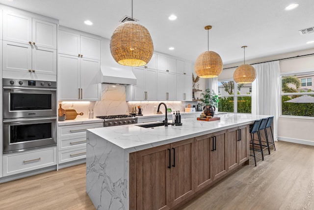 kitchen with appliances with stainless steel finishes, sink, an island with sink, and white cabinets