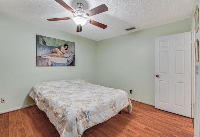 bedroom with ceiling fan, wood-type flooring, and a textured ceiling