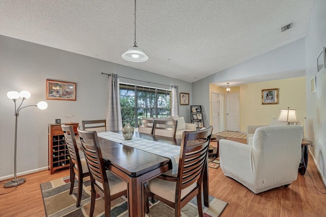 dining room featuring light hardwood / wood-style flooring, vaulted ceiling, and a textured ceiling