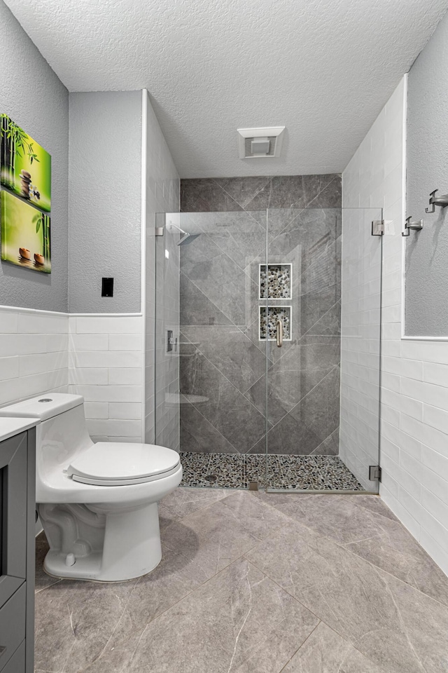 bathroom featuring tile walls, vanity, toilet, a shower with door, and a textured ceiling