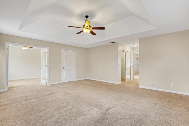 spare room featuring ceiling fan, a raised ceiling, and light carpet